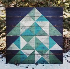 a blue and green wooden block sitting in the snow next to some pine tree branches