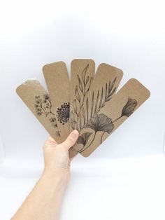 a hand holding four brown paper tags with flowers on them and leaves in the middle