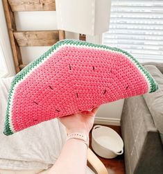 a person holding up a crocheted watermelon pillow in front of a couch