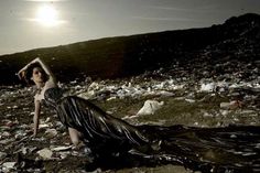 a woman sitting on top of a pile of trash next to a mountain covered in garbage