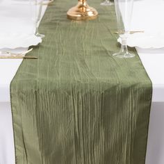 the table is set with white plates and silverware, gold utensils and an olive green linen runner