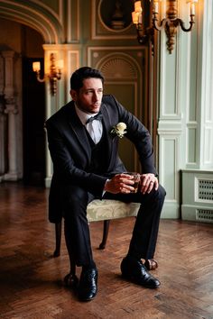 a man in a tuxedo is sitting on a chair and holding a flower