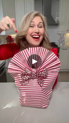 a woman is holding up a red and white striped box with a bow on it