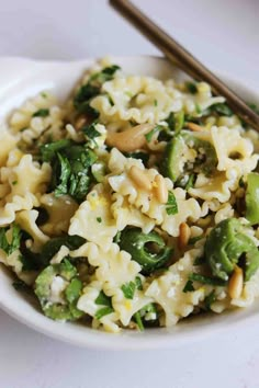 a white bowl filled with pasta and vegetables next to chopsticks on a table