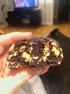 a hand holding a half eaten chocolate and peanut butter cookie in front of a tv