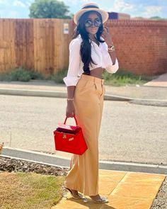 a woman in white shirt and tan pants holding a red bag