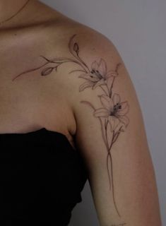 a woman wearing a black dress with flowers on her shoulder and arm tattooing it