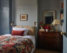 a bed sitting next to a dresser with a mirror on top of it and a lamp