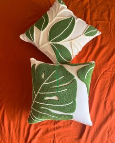 two green and white pillows sitting on top of an orange bed cover covered in leaves