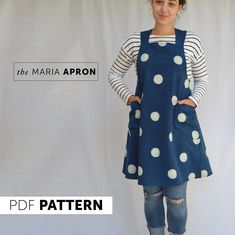 a woman standing in front of a white backdrop wearing a blue polka dot apron and jeans