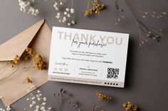 a thank you card sitting on top of an envelope next to dried flowers and paper