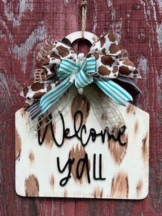 a welcome you sign hanging on the side of a wooden door with a blue and white bow