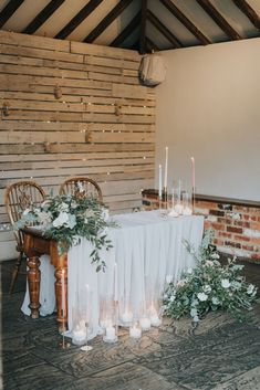 a table with candles, flowers and greenery is set up in front of a brick wall