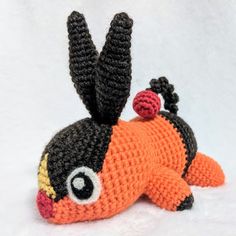 an orange and black crocheted stuffed animal laying on the ground with its eyes open