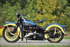 a blue and yellow motorcycle parked on the side of a road next to some trees