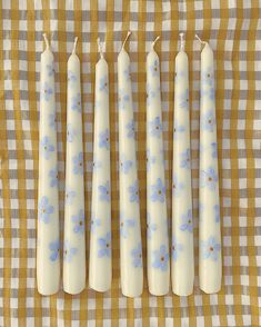 four candles with blue flowers on them sitting on a checkered tablecloth covered cloth