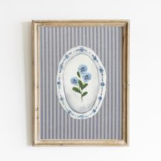 a painting with blue flowers in a oval frame on a white wall next to a striped wall