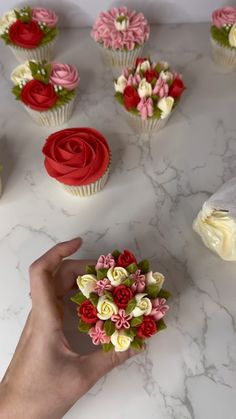 cupcakes decorated with flowers are being held by a person's hand on a marble surface