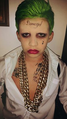 a woman with green hair and tattoos on her face, wearing gold chain necklaces