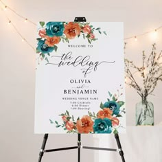 a welcome sign with flowers on it in front of a white backdrop and string lights