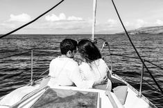 a man and woman sitting on the back of a sailboat looking out at the ocean