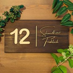 a wooden sign with the number twelve on it next to some leaves and flowers in front of it