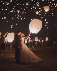 a bride and groom are holding lanterns in the air as they fly through the night sky