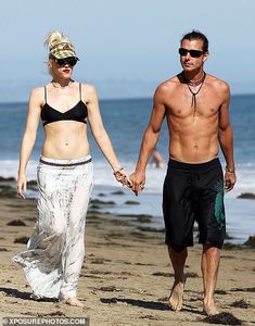 the man and woman are walking on the beach holding hands while wearing swimsuits