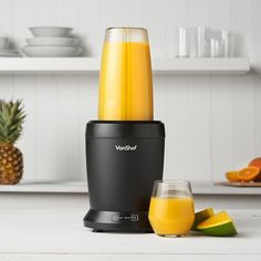 a black blender sitting on top of a counter next to sliced oranges and pineapple