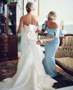 two women in dresses standing next to each other and looking at the bride's dress