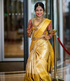 a woman in a yellow sari holding a gold pole and smiling at the camera