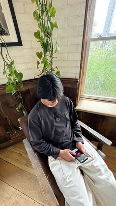 a person sitting on a bench with a cell phone in their hand and a potted plant behind them