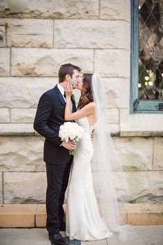 a bride and groom kissing in front of a stone building