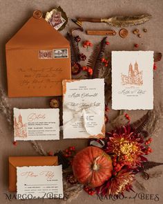 the wedding stationery is laid out on top of an orange and white envelope, surrounded by autumn foliage