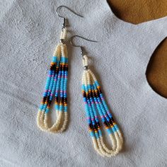 a pair of beaded earrings on top of a white shirt next to a piece of fabric