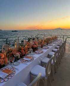 a long table is set up on the beach for an outdoor dinner with candles and flowers