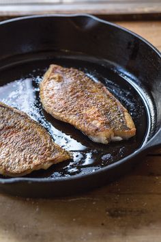 two pieces of fish are cooking in a skillet