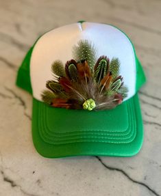 This beautiful green & white trucker hat with green and natural colored feathers, and a green stone embellishment will be all anyone can talk about when you wear it.  It's such a fun way to spice up any outfit and the places to wear this hat are endless. Be prepared for loads of compliments.  The feathers are handpicked for each hat.  The hat has a foam front, mesh back, and an adjustable snap back. Green Trucker Hat For Spring, One Size Fits Most, Green Spring Trucker Hat, Adjustable Brimmed Green Mini Hats, Green Adjustable Trucker Hat For Spring, Adjustable Green Trucker Hat With Short Brim, Adjustable Green Brimmed Mini Hats, Green Adjustable Trucker Hat With Short Brim, Green Baseball Cap As Gift, Adjustable Green Mini Hats For Summer