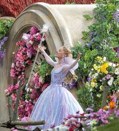 a woman dressed in a blue and white dress holding a wand with flowers around her