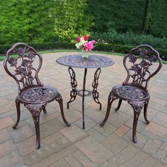 an outdoor table and two chairs on a brick patio with flowers in the vase at the end