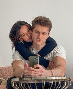 a man and woman sitting on top of a bed looking at a cell phone together