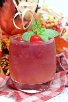 a drink with a cherry and mint garnish on the rim is sitting on a checkered tablecloth