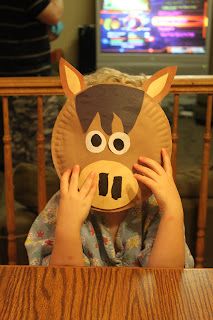 a young boy is covering his face with a paper plate horse mask in front of him