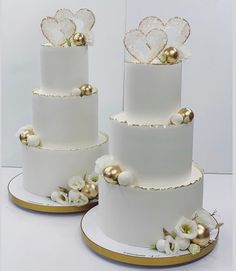 three tiered white wedding cake with gold decorations and flowers on each layer, sitting next to each other