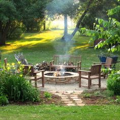 a fire pit surrounded by wooden chairs in the middle of a yard with grass and trees