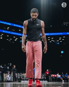 a man standing on top of a basketball court wearing pink pants and red shoes with his hands in his pockets