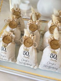 small bags filled with wedding favors on top of a glass tray next to a gold chain