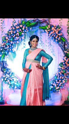 a woman in a pink and blue sari standing next to a floral display with flowers