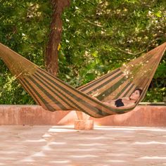 a woman laying in a hammock on the ground next to a tree and some bushes