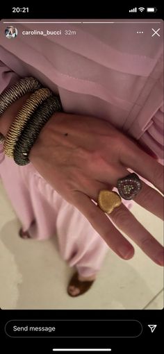 a woman's hand with rings and bracelets on her wrist, wearing a pink dress